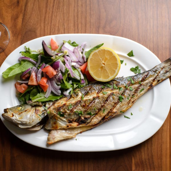 Grilled whole fish with a side salad of greens, red onion, and tomato, garnished with lemon.