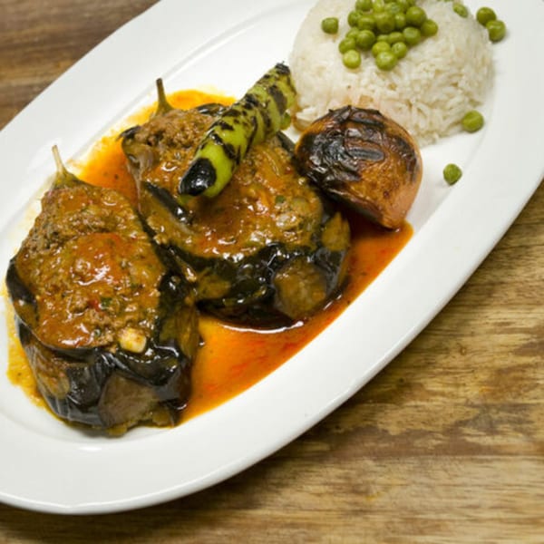 Mediterranean stuffed eggplant with rice and peas, garnished with grilled pepper and onion.