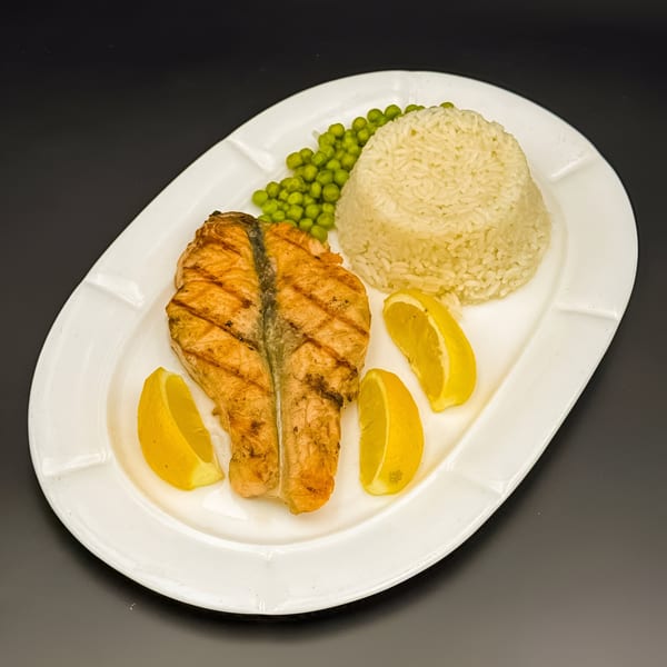 Grilled salmon fillet with rice, green peas, and lemon wedges on a white plate.