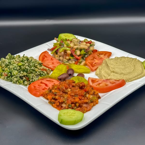 A white square plate filled with various Mediterranean appetizers, including hummus, tabbouleh, and bean salad.