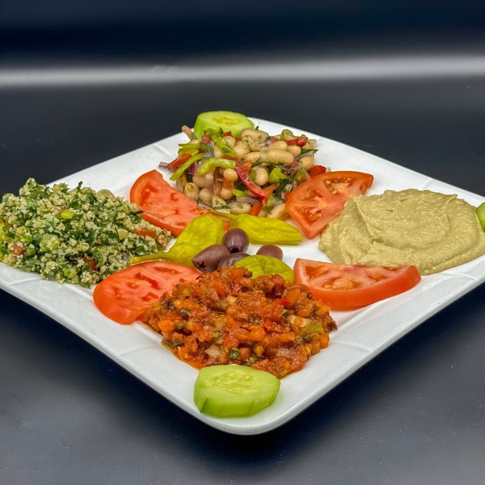 A white square plate filled with various Mediterranean appetizers, including hummus, tabbouleh, and bean salad.