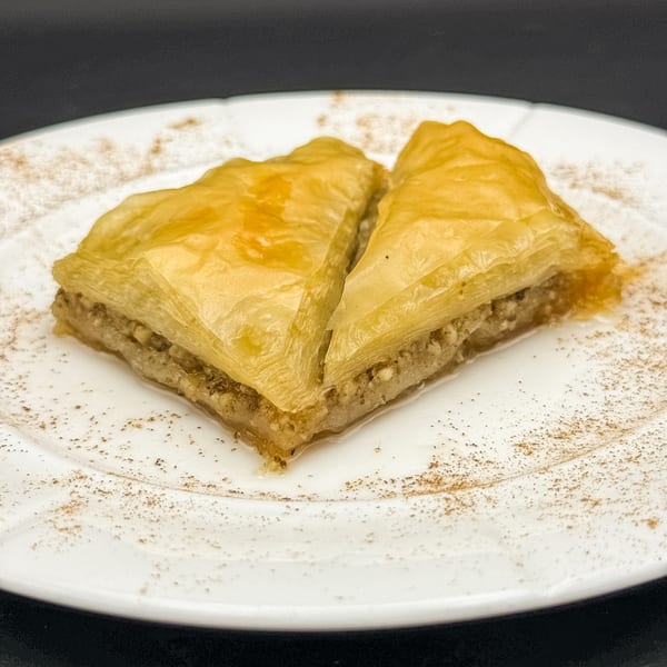 Two pieces of golden-brown baklava with nuts and honey, dusted with cinnamon on a white plate.