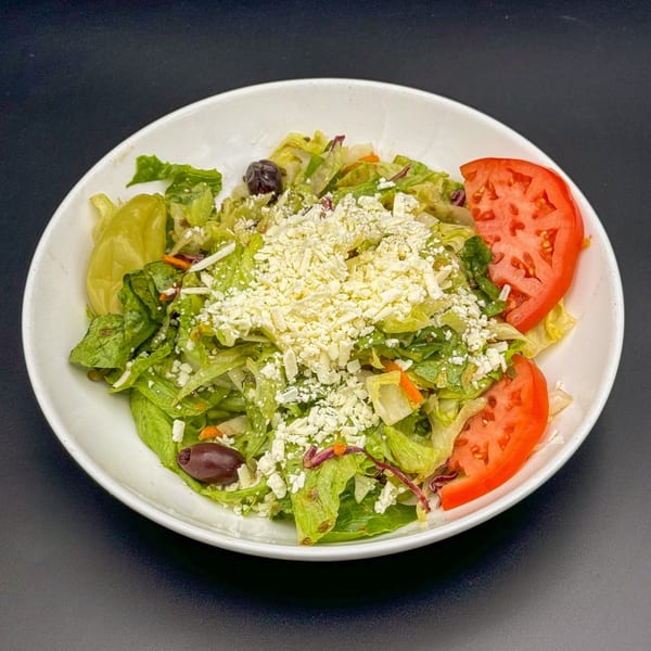 A fresh Mediterranean salad with lettuce, tomatoes, olives, and crumbled feta cheese in a white bowl.