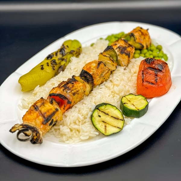 Grilled chicken kebab with rice, zucchini, tomato, and a green pepper on a white plate.